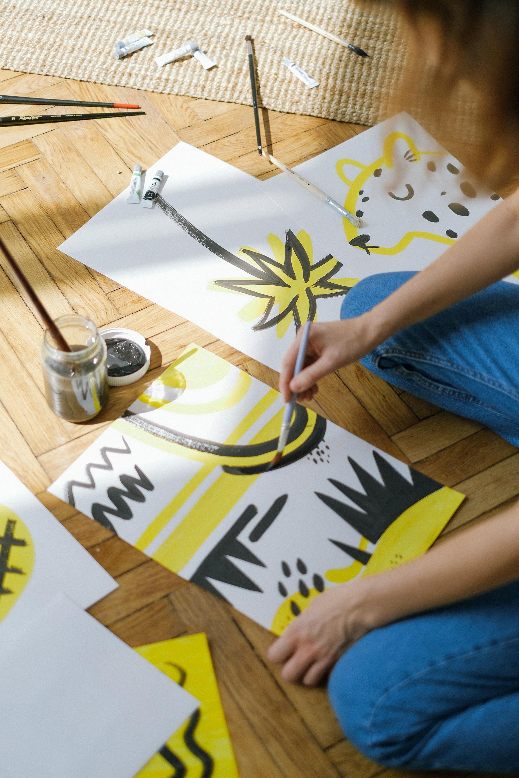A person painting abstract designs on paper in a bright, artistic studio.